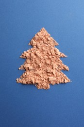 Photo of Christmas tree made with face powder on blue background, top view