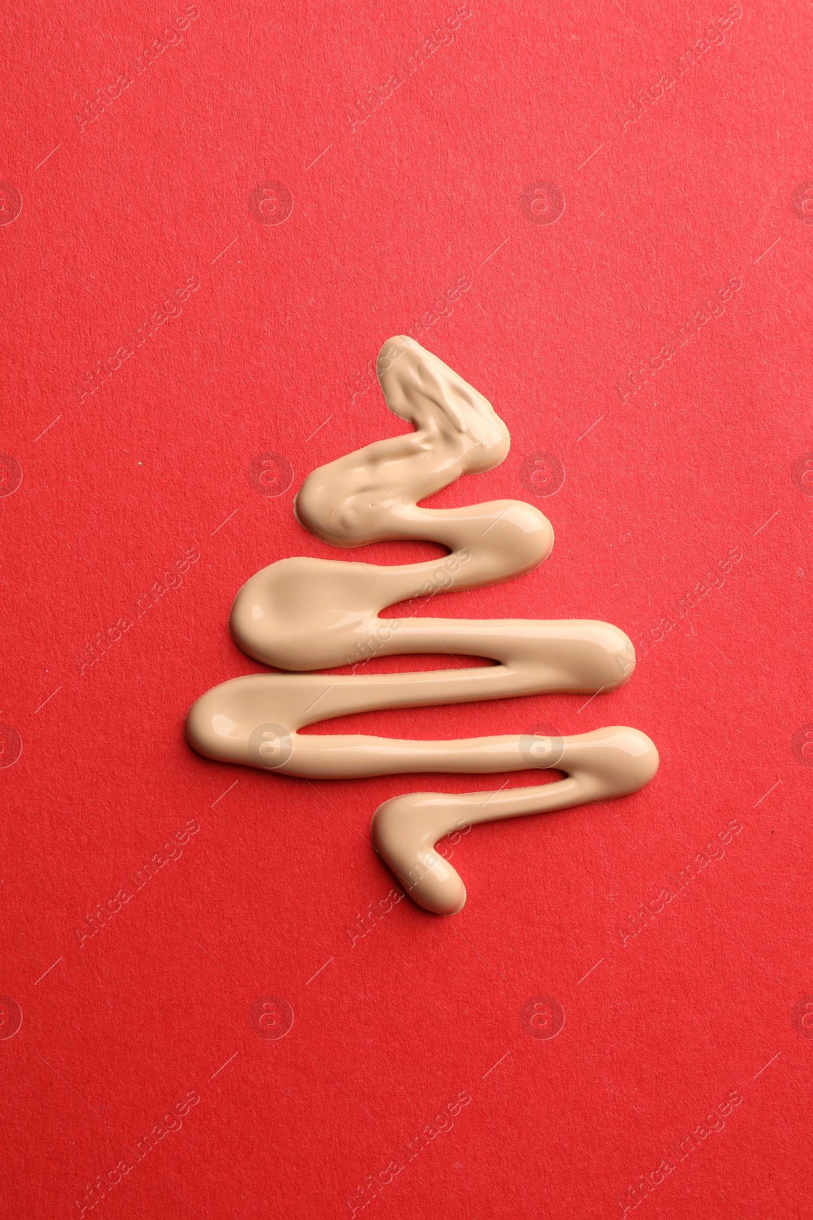 Photo of Christmas tree made of skin foundation on red background, top view