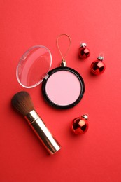 Photo of Blusher in shape of Christmas ball and brush on red background, flat lay