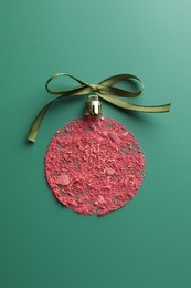 Photo of Christmas ball made of blush and bow on green background, top view