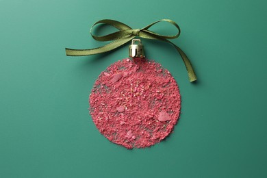 Photo of Christmas ball made of blush and bow on green background, top view