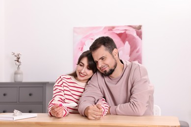 Photo of Happy young couple with pregnancy test at wooden table indoors