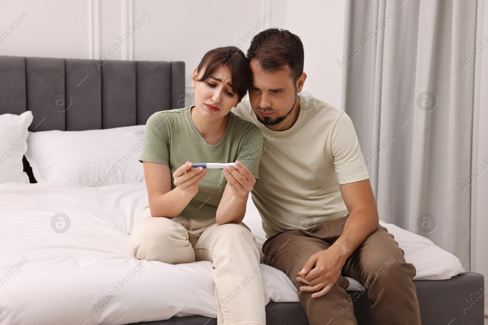 Photo of Worried young couple with pregnancy test on bed at home