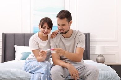 Photo of Happy young couple with pregnancy test on bed at home