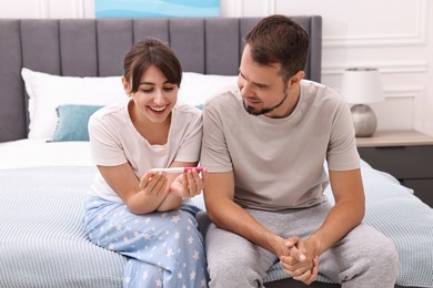 Photo of Happy young couple with pregnancy test on bed at home