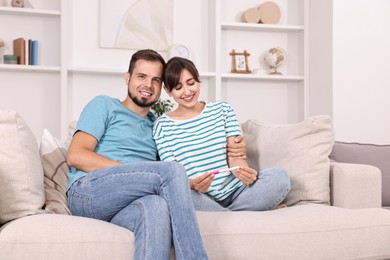 Photo of Happy young couple with pregnancy test on sofa at home