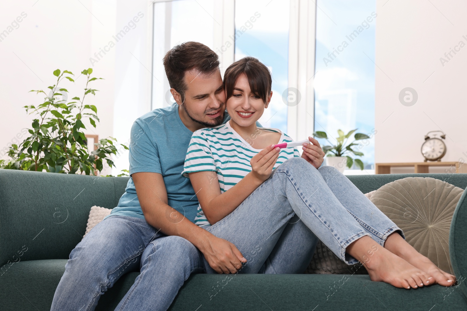 Photo of Happy young couple with pregnancy test on sofa at home