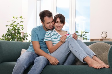 Photo of Happy young couple with pregnancy test on sofa at home