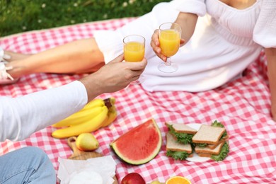 Lovely couple clinking glasses of juice on picnic blanket outdoors, closeup