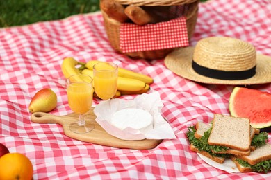 Photo of Different food, juice and hat on picnic blanket outdoors, closeup