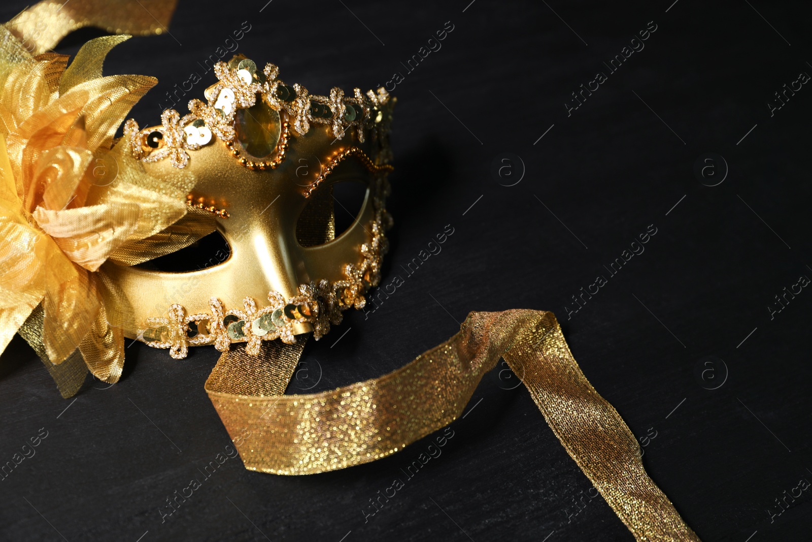 Photo of Beautiful golden carnival mask on black table, space for text