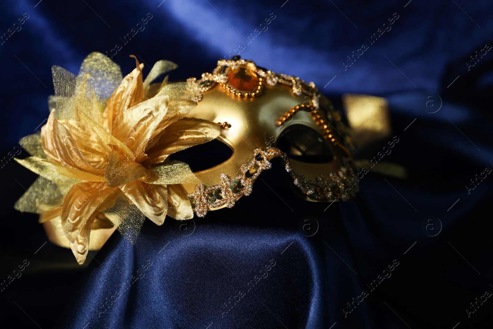 Photo of Beautiful golden carnival mask on blue silk fabric, closeup