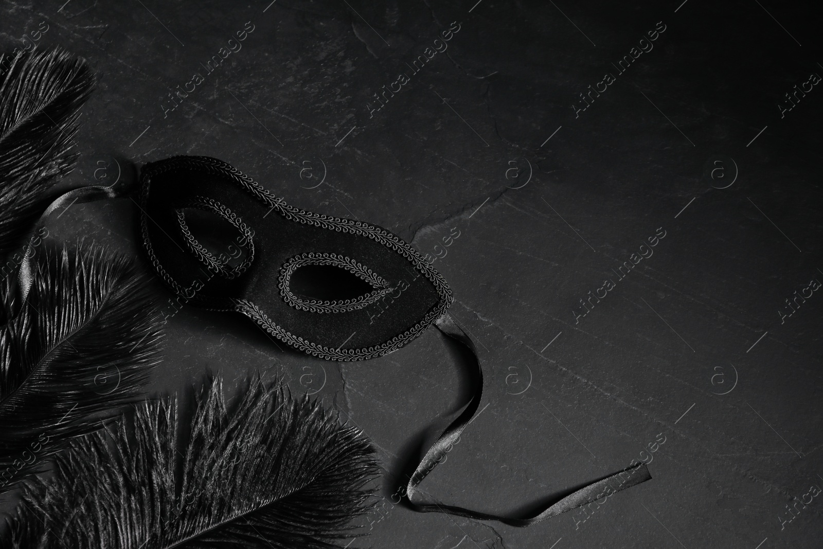 Photo of Beautiful carnival mask and feathers on black table. Space for text