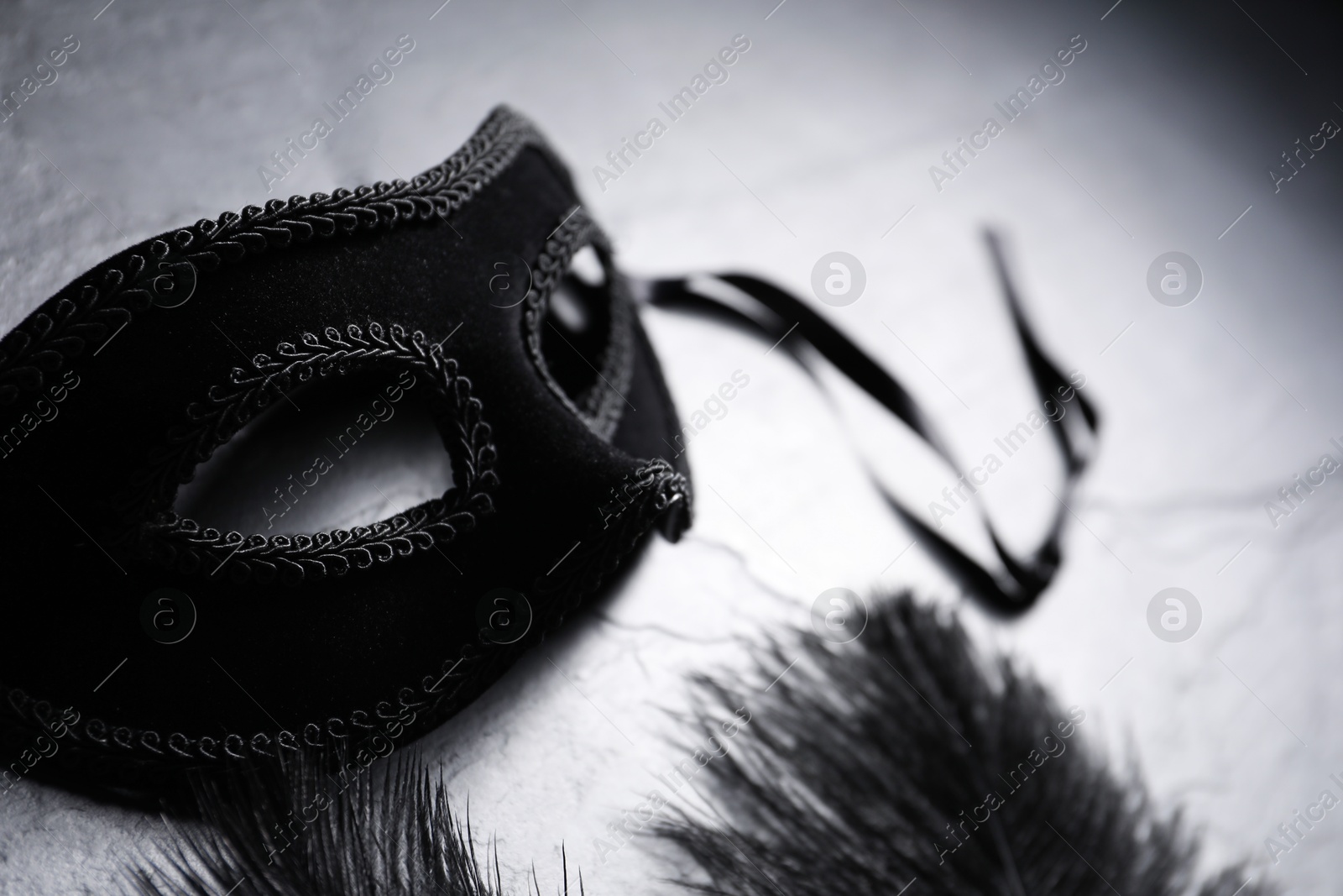 Photo of Beautiful carnival mask and feathers on grey table, closeup