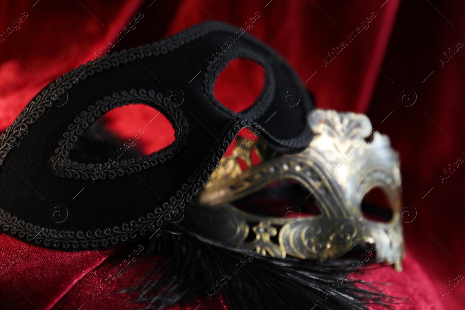 Photo of Beautiful carnival masks on red silk fabric, closeup