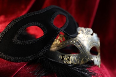 Photo of Beautiful carnival masks on red silk fabric, closeup