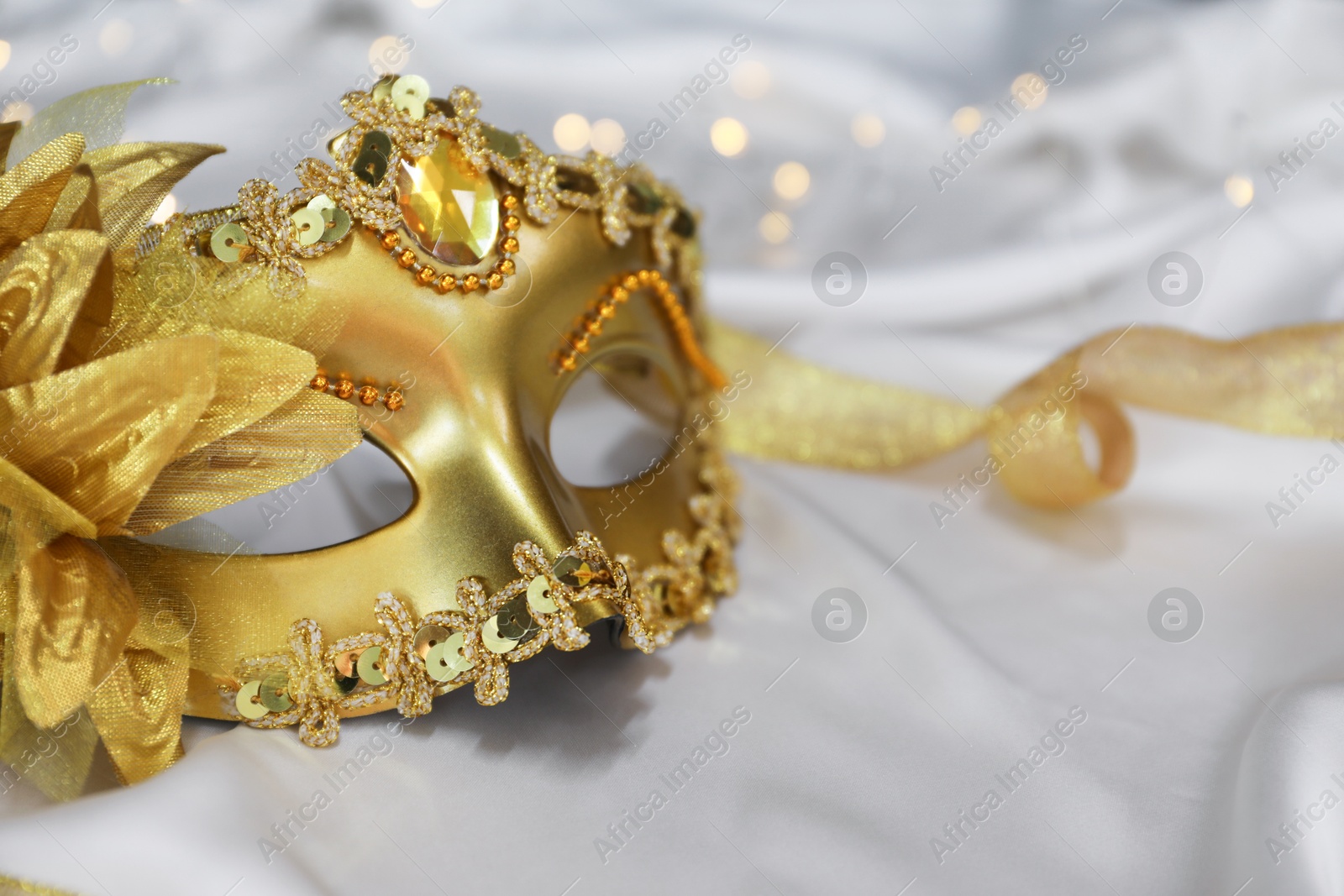 Photo of Beautiful golden carnival on white silk fabric, closeup