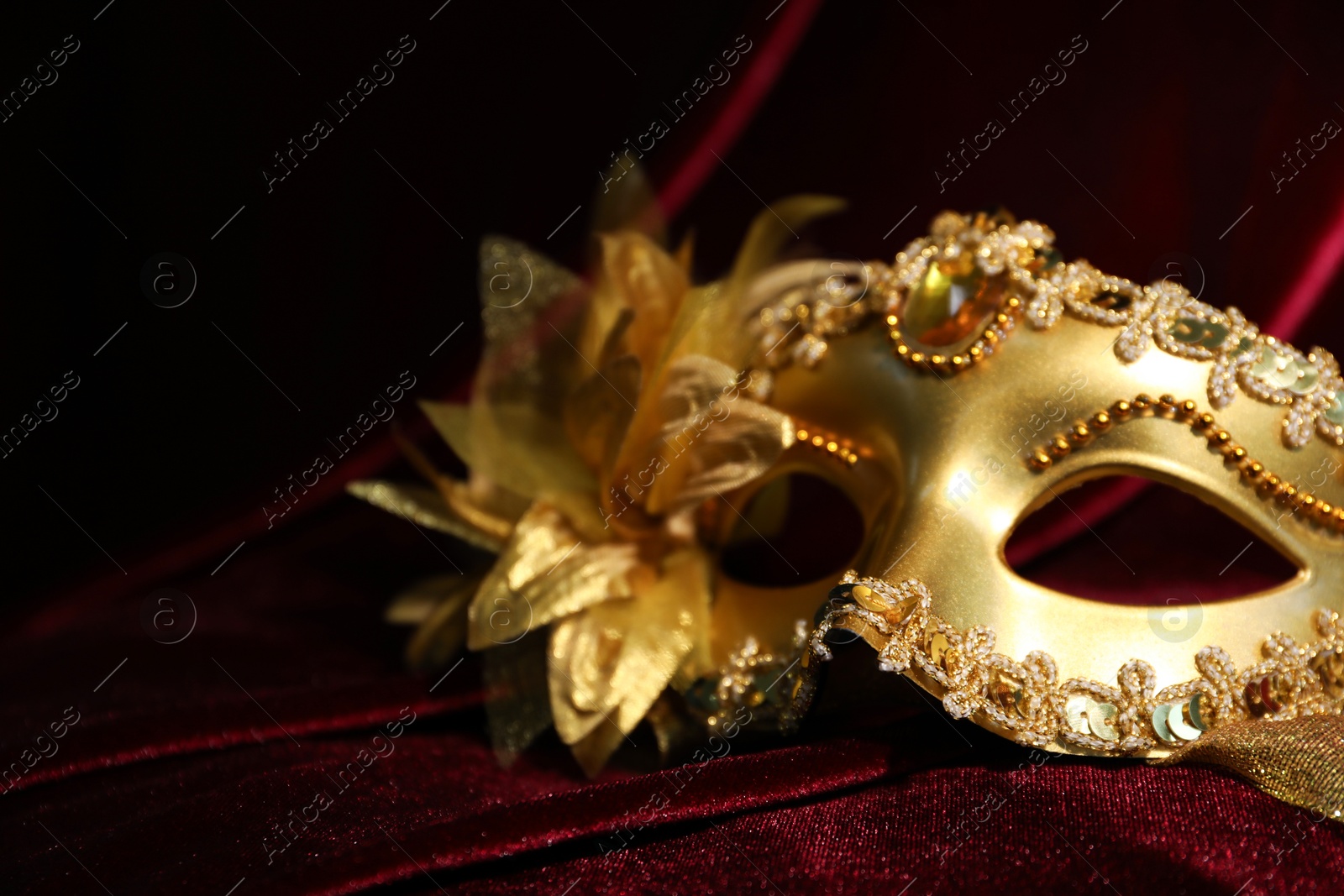 Photo of Beautiful golden carnival mask on red silk fabric, closeup