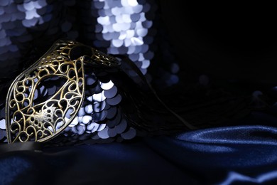 Beautiful carnival mask and fabric with golden sequins in darkness, closeup. Space for text