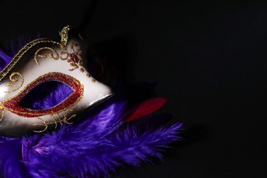 Beautiful carnival mask and bright feathers on black background, closeup. Space for text