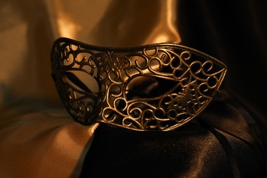 Photo of Beautiful golden carnival mask on silk fabric, closeup