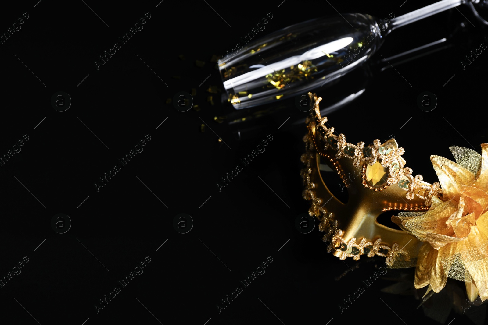 Photo of Beautiful golden carnival mask and champagne glass on black background. Space for text