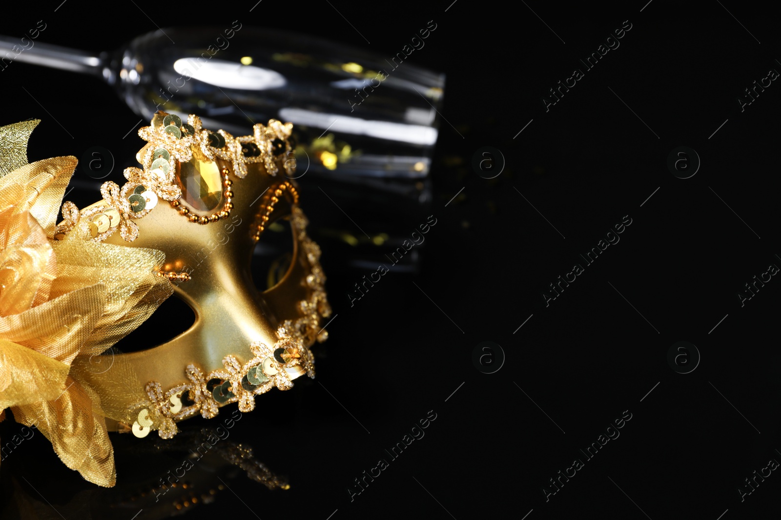 Photo of Beautiful golden carnival mask and champagne glass on black background. Space for text