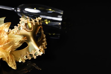 Beautiful golden carnival mask and champagne glass on black background. Space for text