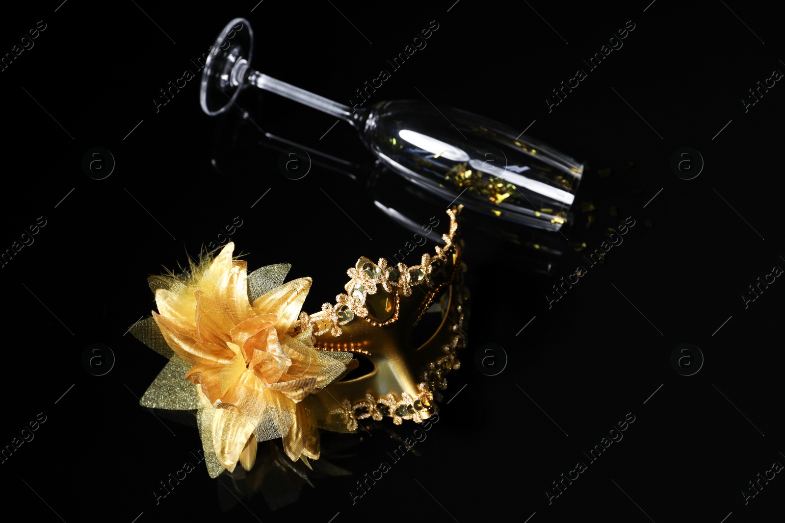 Photo of Beautiful golden carnival mask and champagne glass on black background