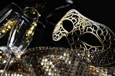 Photo of Beautiful carnival masks, champagne, glasses and fabric with golden sequins on black background, closeup