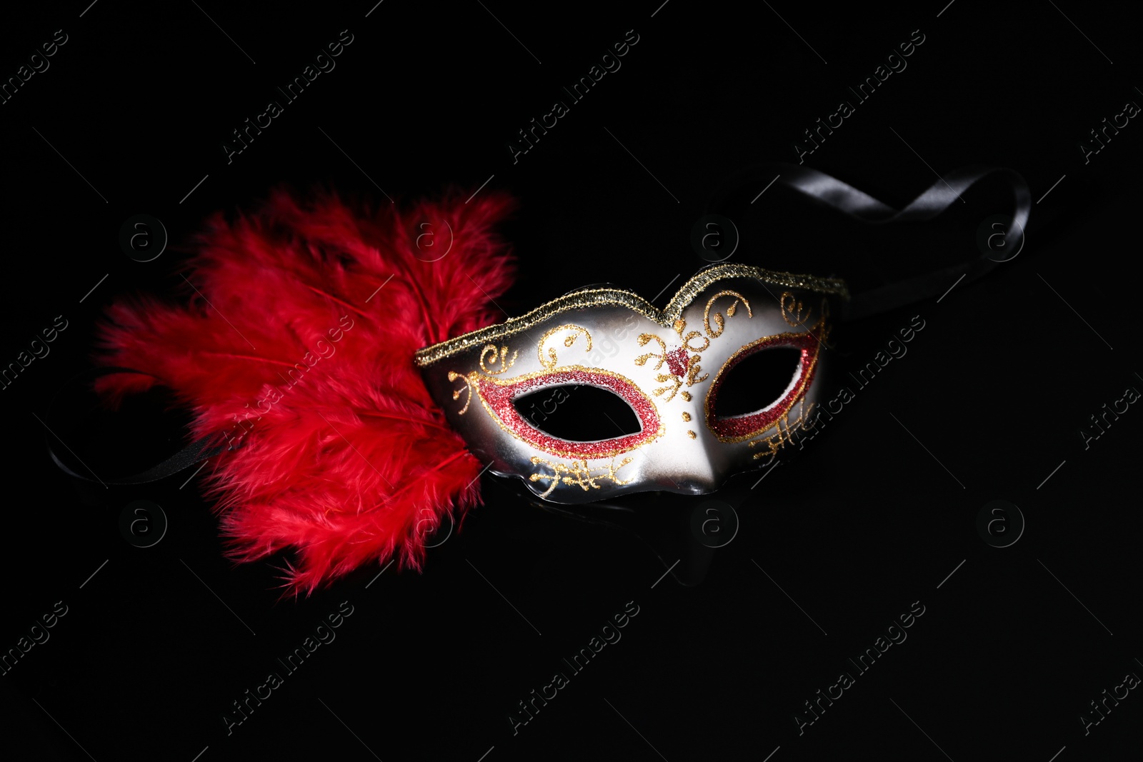 Photo of Beautiful carnival mask in darkness, closeup view