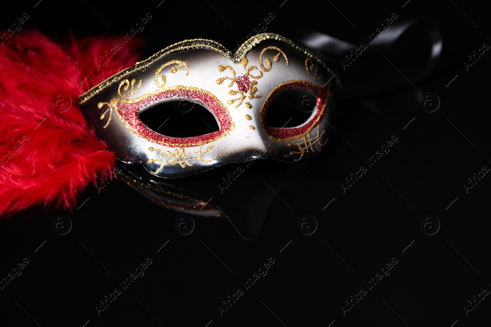 Photo of Beautiful carnival mask in darkness, closeup view. Space for text