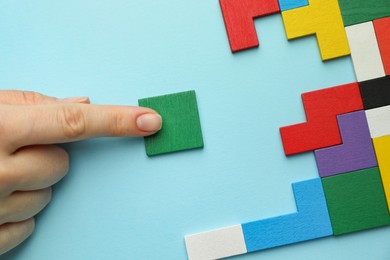 Photo of Woman playing with colorful wooden puzzle pieces on light blue background, top view