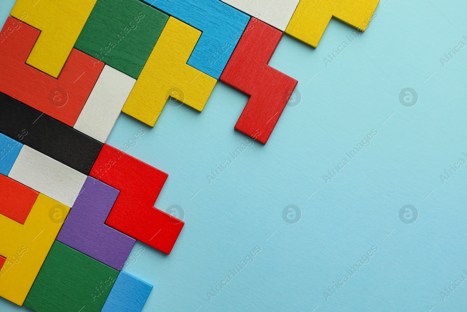 Photo of Colorful wooden puzzle pieces on light blue background, top view. Space for text