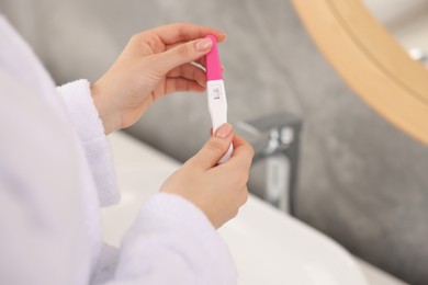 Woman holding pregnancy test in bathroom, closeup. Space for text