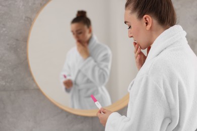 Photo of Woman holding pregnancy test near mirror in bathroom