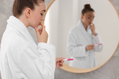 Photo of Woman holding pregnancy test near mirror in bathroom