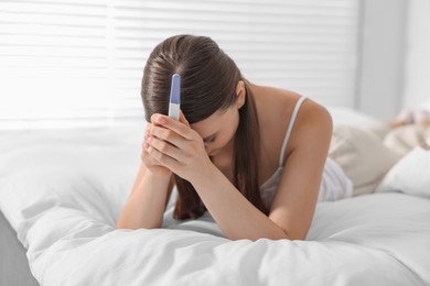 Sad woman holding pregnancy test on bed in room