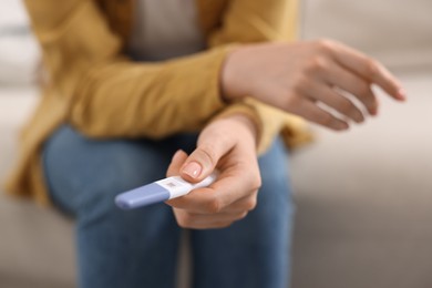 Photo of Woman holding pregnancy test on sofa indoors, closeup