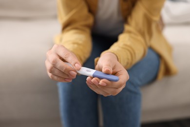 Photo of Woman holding pregnancy test on sofa indoors, closeup