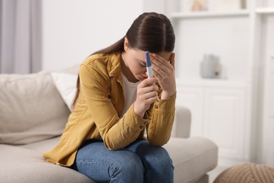 Photo of Sad woman holding pregnancy test on sofa indoors, space for text