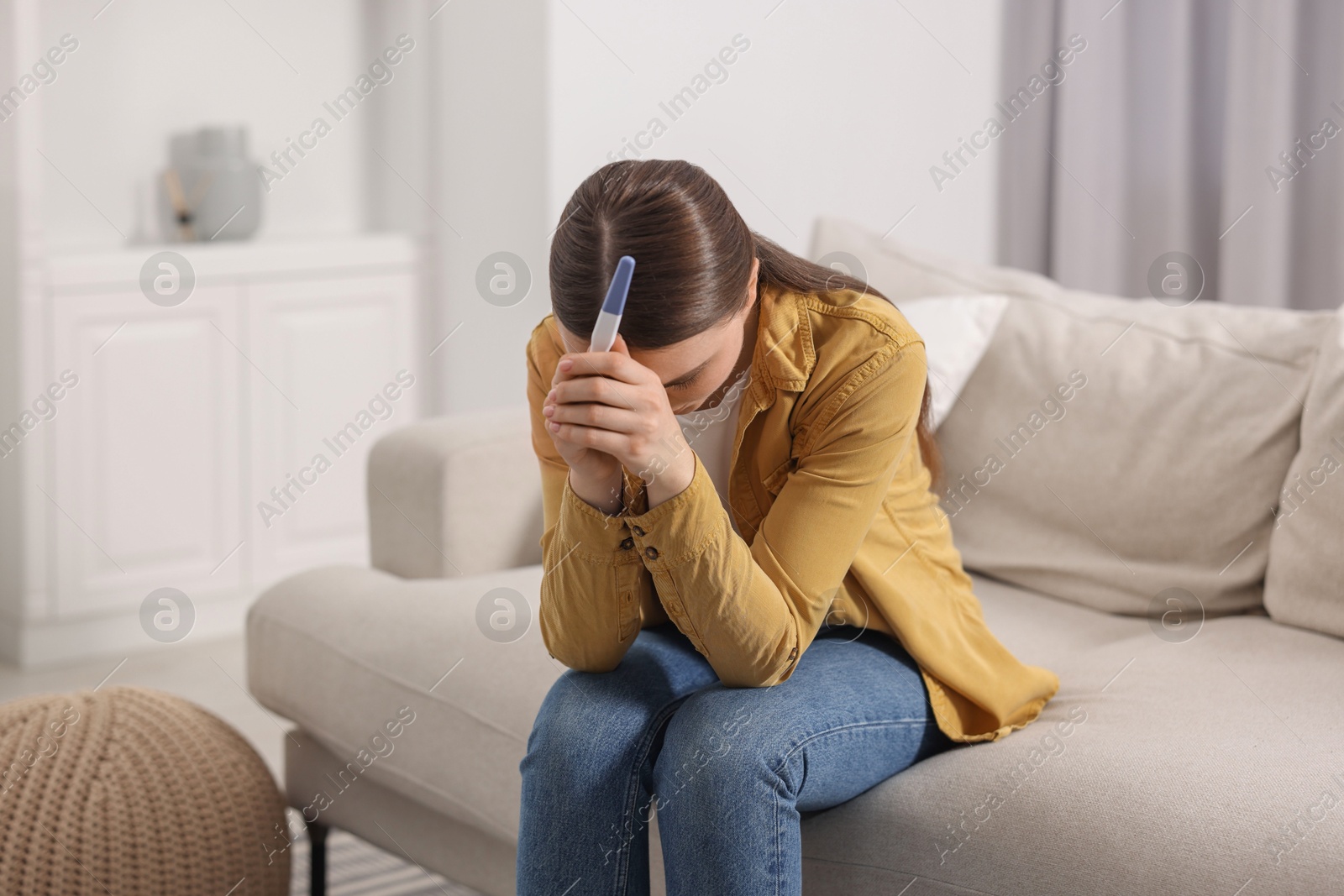 Photo of Sad woman holding pregnancy test on sofa indoors, space for text