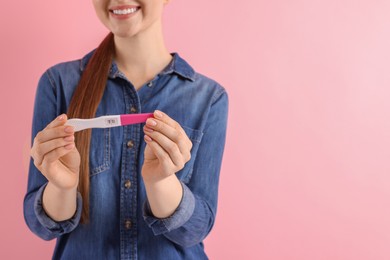 Woman holding pregnancy test on pink background, closeup. Space for text