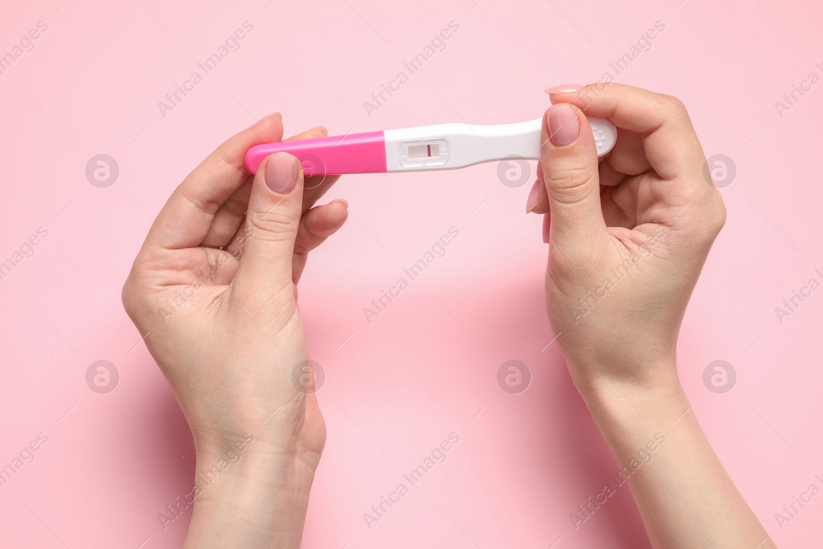 Photo of Woman holding pregnancy test on pink background, closeup