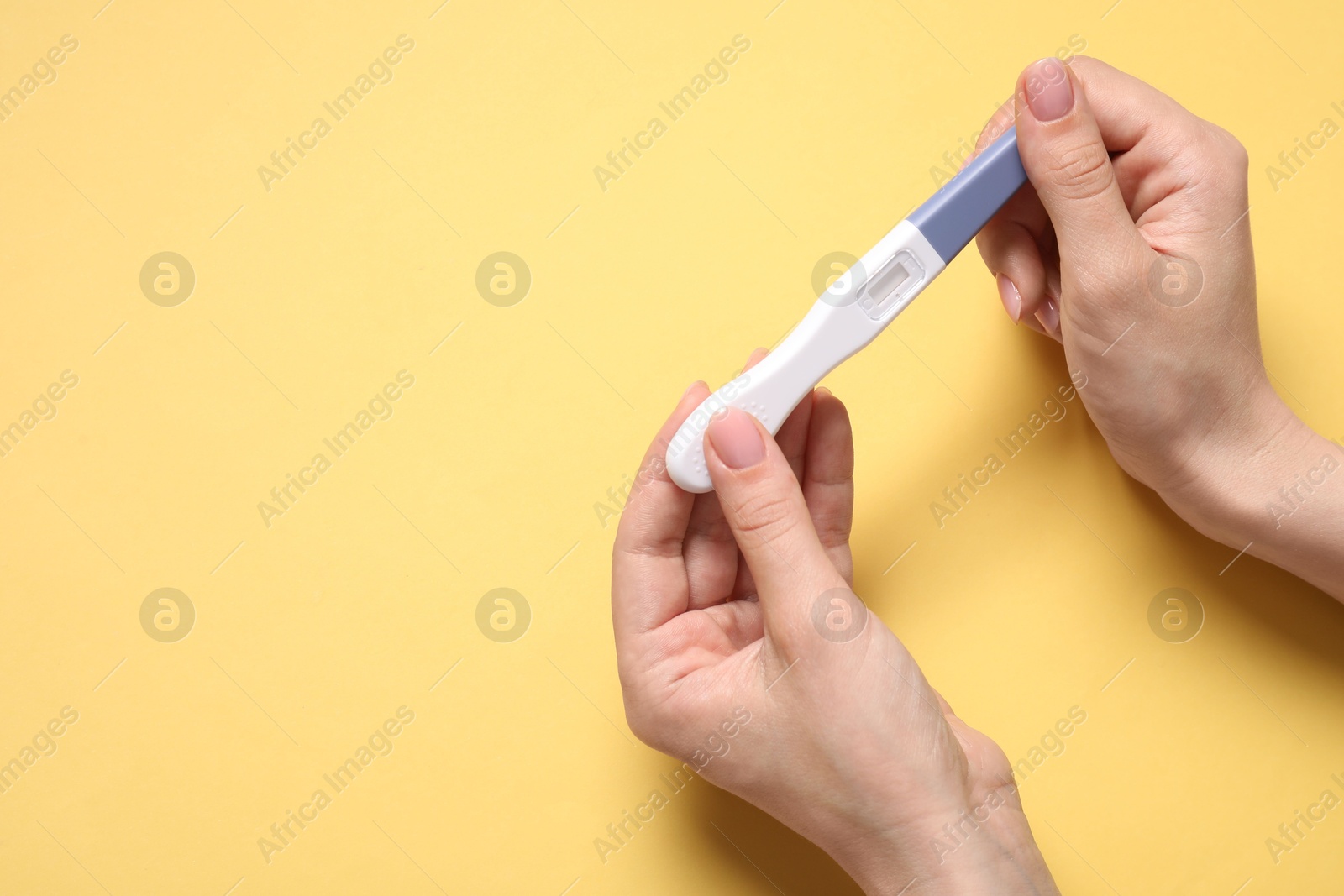 Photo of Woman holding pregnancy test on yellow background, closeup. Space for text