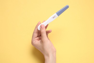 Photo of Woman holding pregnancy test on yellow background, top view