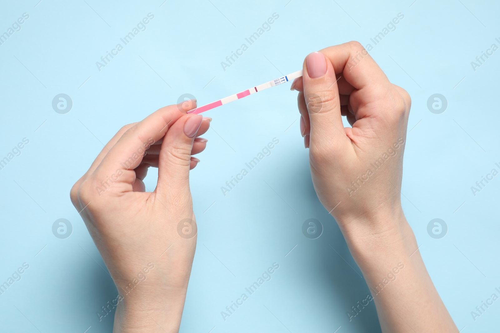 Photo of Woman holding pregnancy test on light blue background, top view