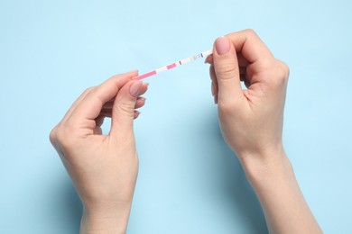 Photo of Woman holding pregnancy test on light blue background, top view