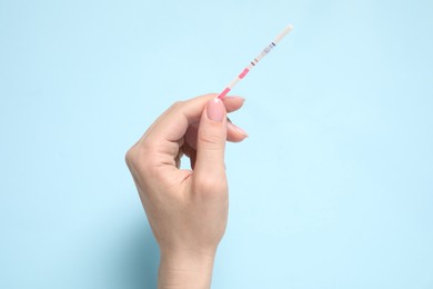 Photo of Woman holding pregnancy test on light blue background, top view