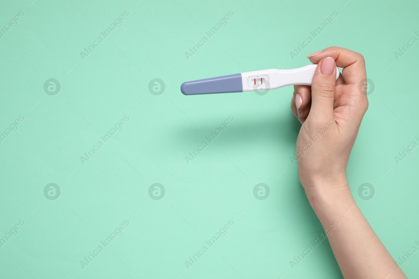 Photo of Woman holding pregnancy test on turquoise background, top view. Space for text